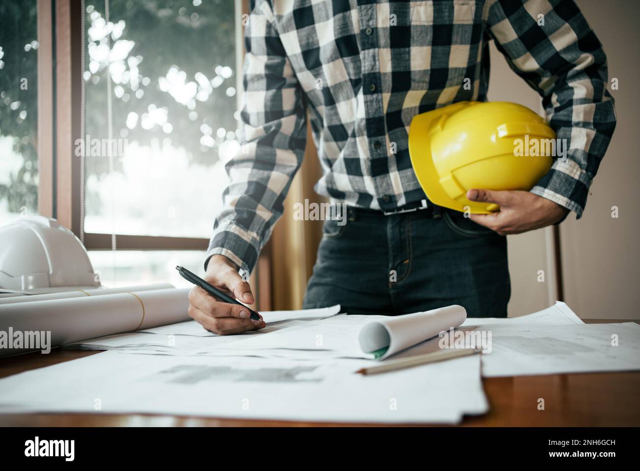 Close-up of asian male civil engineer working on blueprint architecture project on construction site at work desk in office. Stock Photo