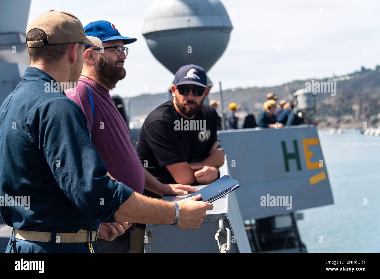 220720-N-VQ947-1046 SAN DIEGO (July 20, 2022) — Ensign Austen Cowper, left, speaks to Steve Walsh, center, a news reporter from KPBS, and Ian Urtnowski, right, from the C4 Foundation and URT Clothing brand, aboard San Antonio-class amphibious transport dock ship USS Portland (LPD 27) as it arrives at the Point Loma fuel pier in San Diego during Rim of the Pacific (RIMPAC) Southern California. Twenty-six nations, 38 ships, three submarines, more than 170 aircraft and 25,000 personnel are participating in RIMPAC from June 29 to Aug. 4 in and around the Hawaiian Islands and Southern California. T Stock Photo