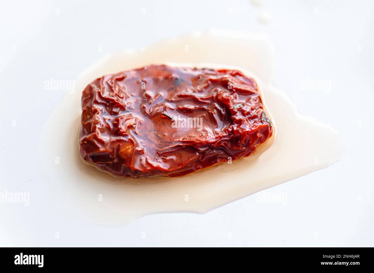 Close-up of one piece dried or sun-dried red tomatoes with oil on white ceramic plate Stock Photo