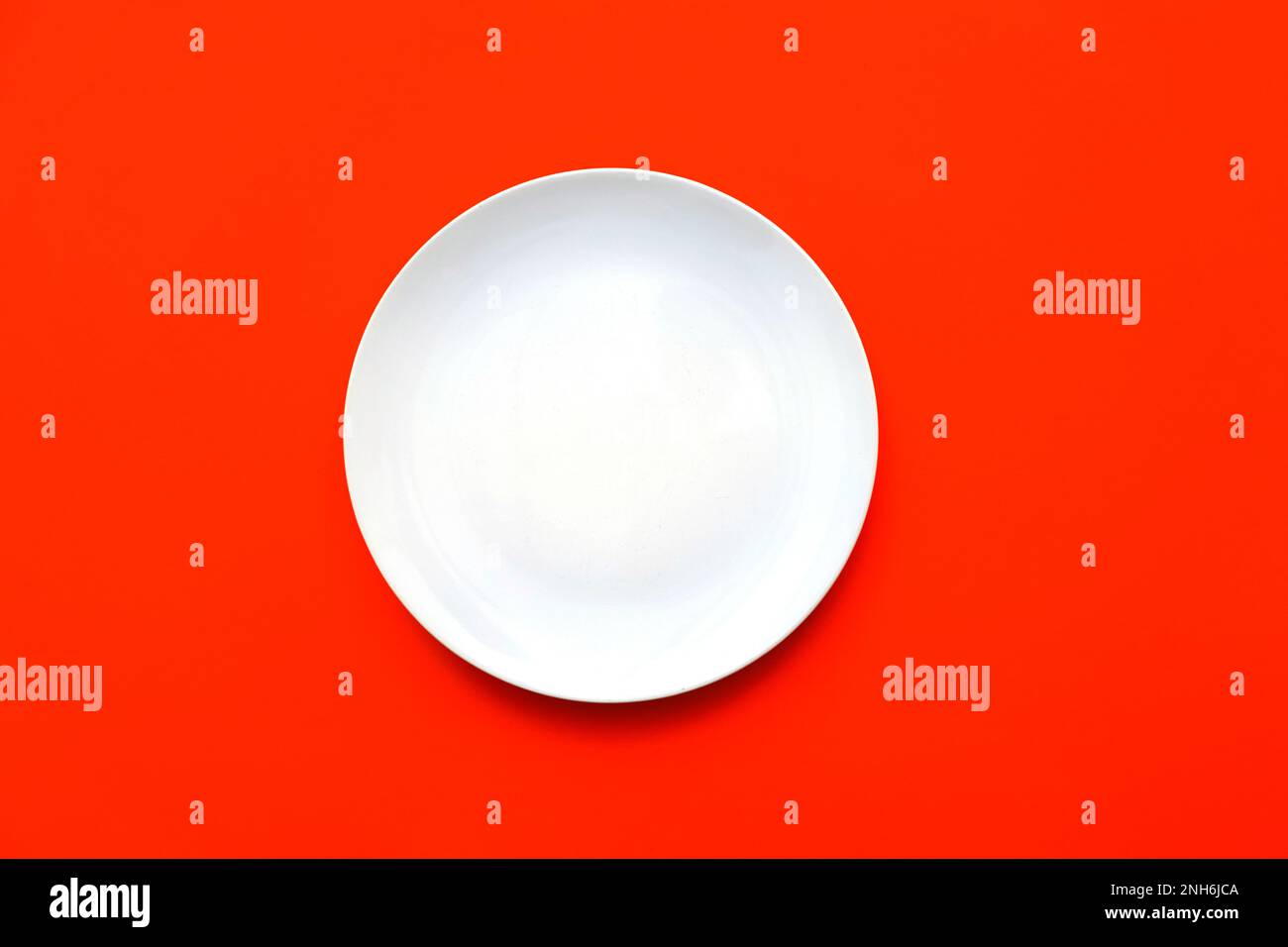 White empty plate with blank surface on bright red backdrop, top view Stock Photo