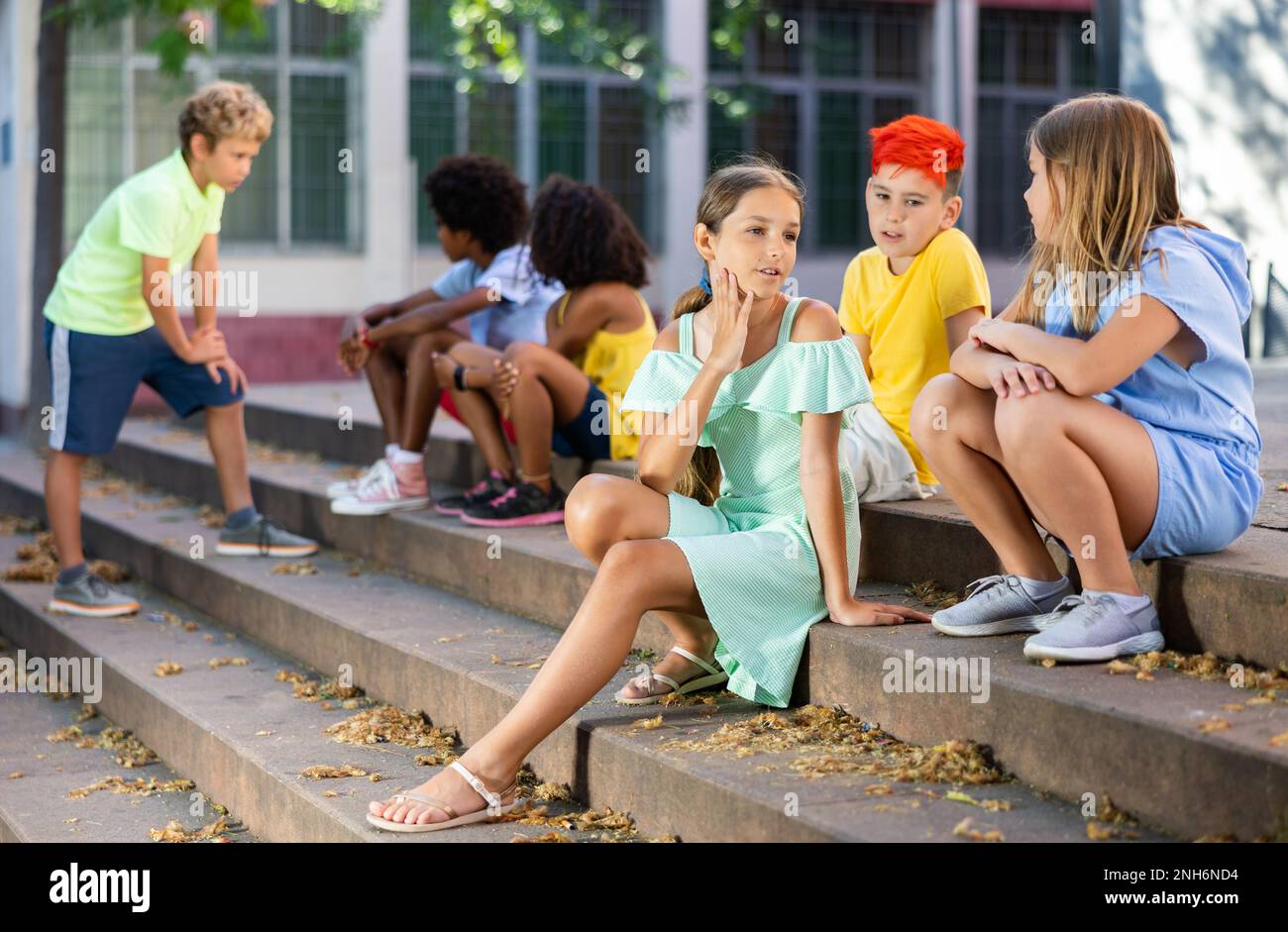 Positive tweenagers friendly blabbing while sitting on steps outdoors Stock Photo