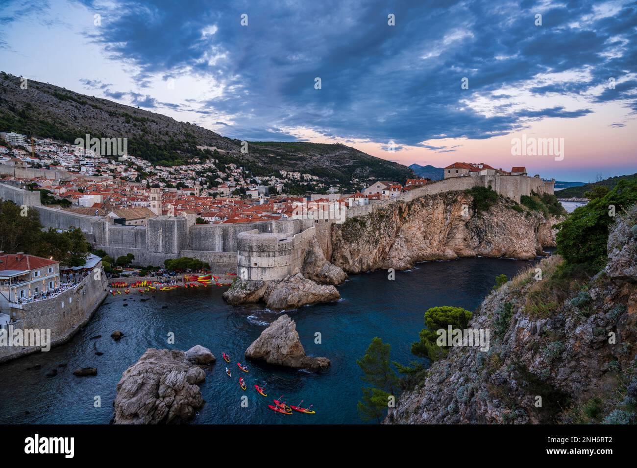 Canoes returning to harbour in Kolorina Bay, with Fort Bokar, town walls and the old town of Dubrovnik in the background, taken at sunset in Croatia Stock Photo