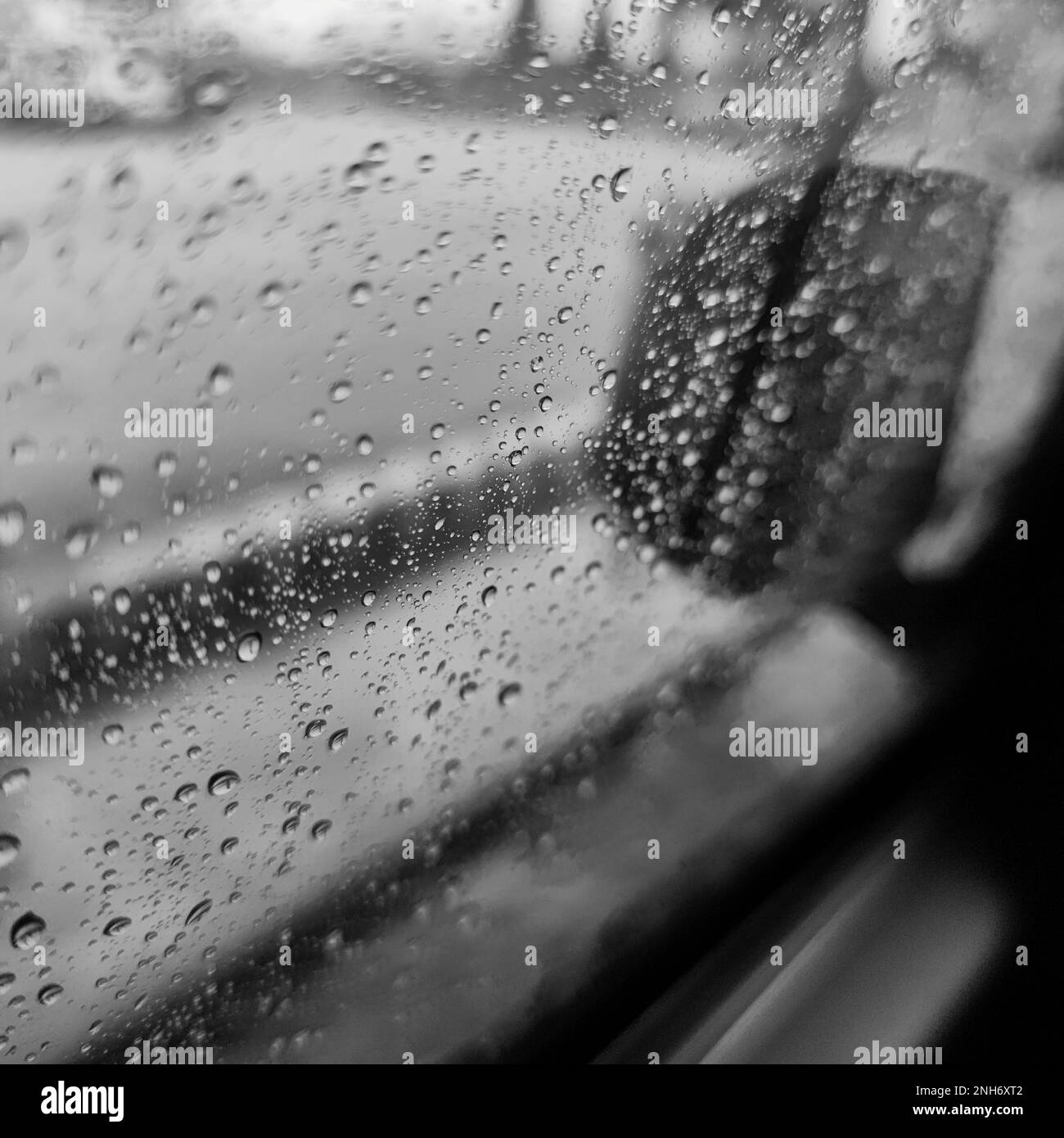 A monochrome photo of a car window with rain drops shot from the inside of the car Stock Photo