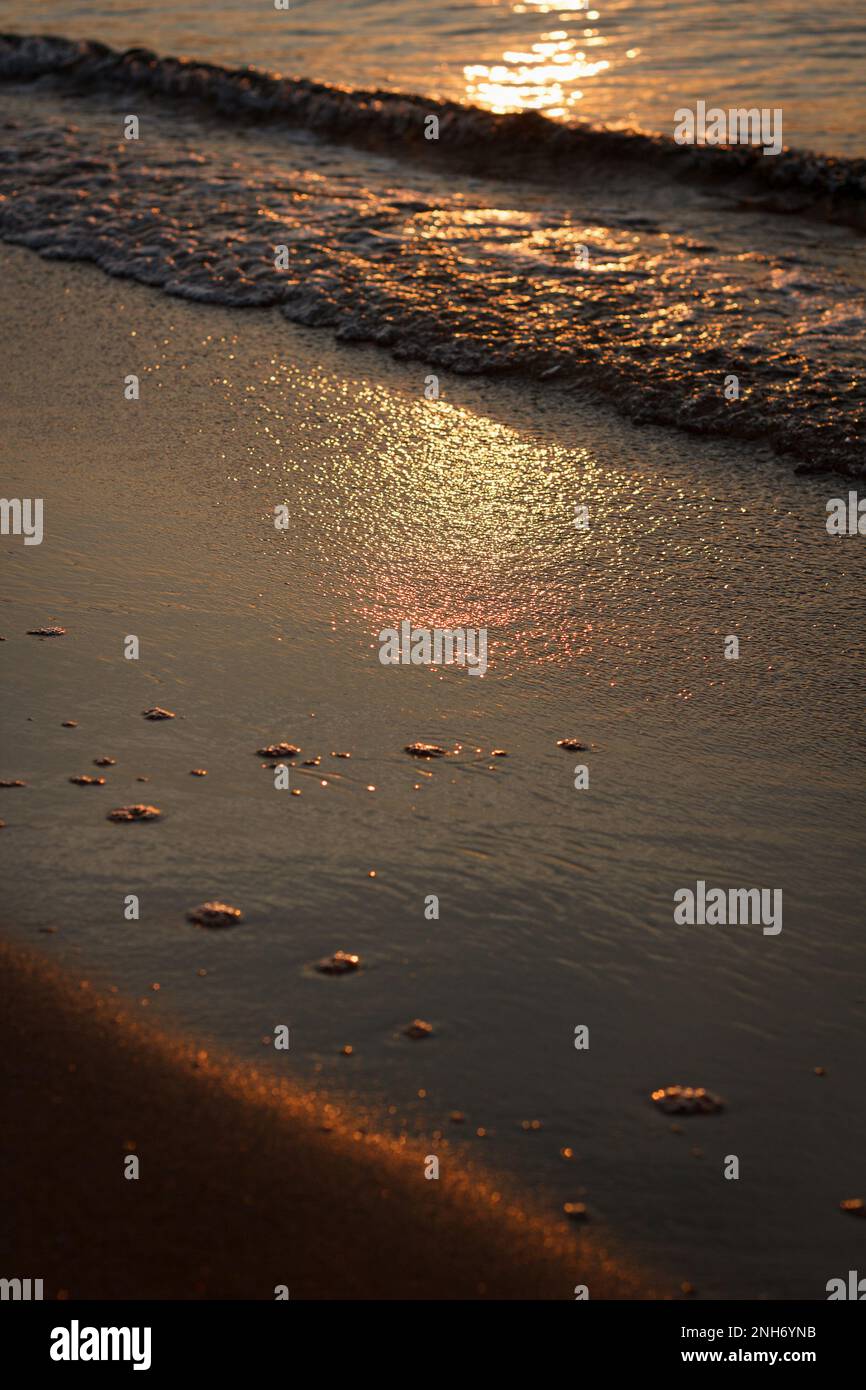 Beautiful sunrise early in the morning at sea, first rays of sun are reflected in waves of black sea and wet sand on shore. Beauty background Stock Photo