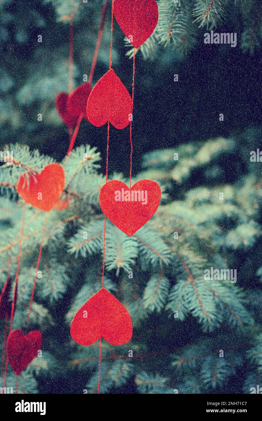 Red decorative beautiful hearts hang on branches of spruce outdoor it is snowing. Beautiful romantic background decorated for Valentine's Day Stock Photo