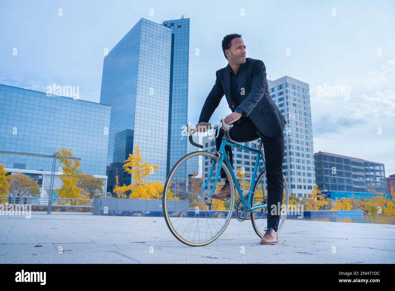 Stylish African American businessman in suit going to the office by bicycle in financial district.  Stock Photo