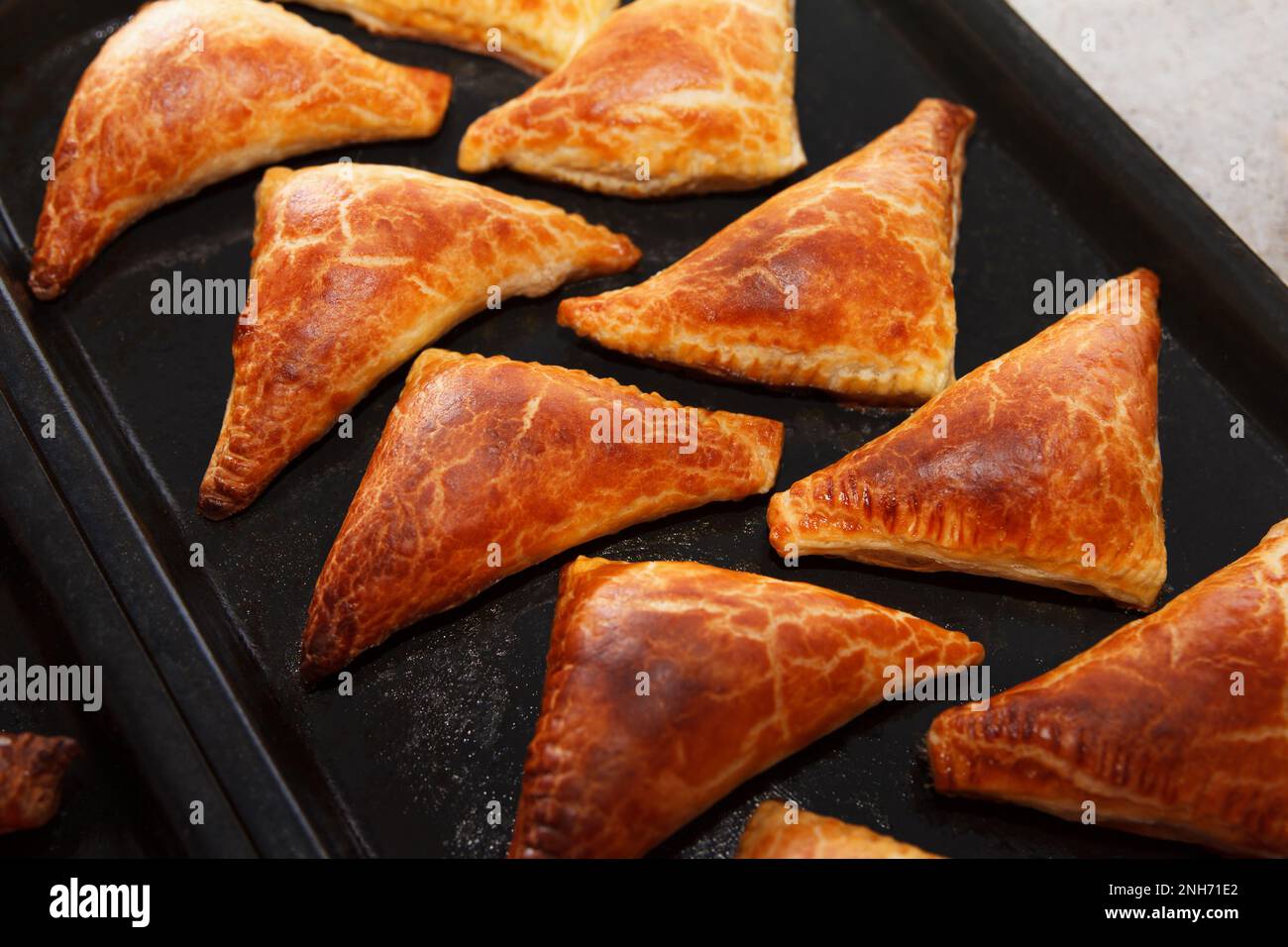Freshly baked delicious hot patties filled with oven, triangular shape lie on a baking sheet Stock Photo