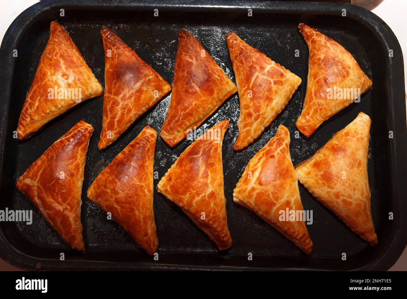 Freshly baked delicious hot patties filled with oven, triangular shape lie on a baking sheet Stock Photo