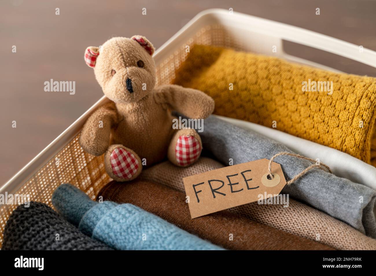 Plastic Box with used clothing and bear toy to donate on wooden table. Reuse. Free label Stock