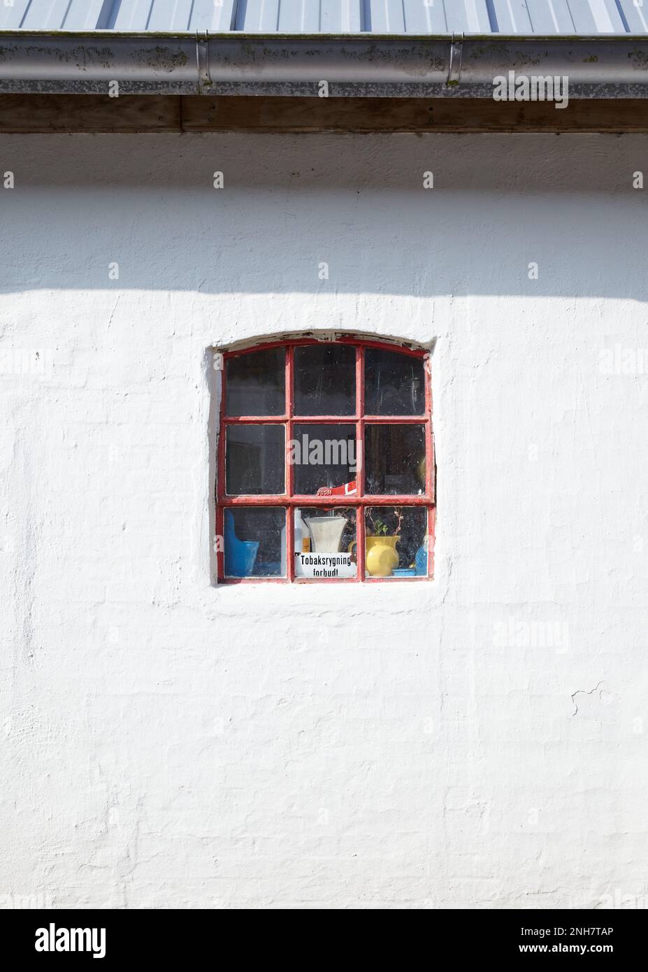 Cosy little white house with a small red window that permits to see objects and a danish sign Stock Photo