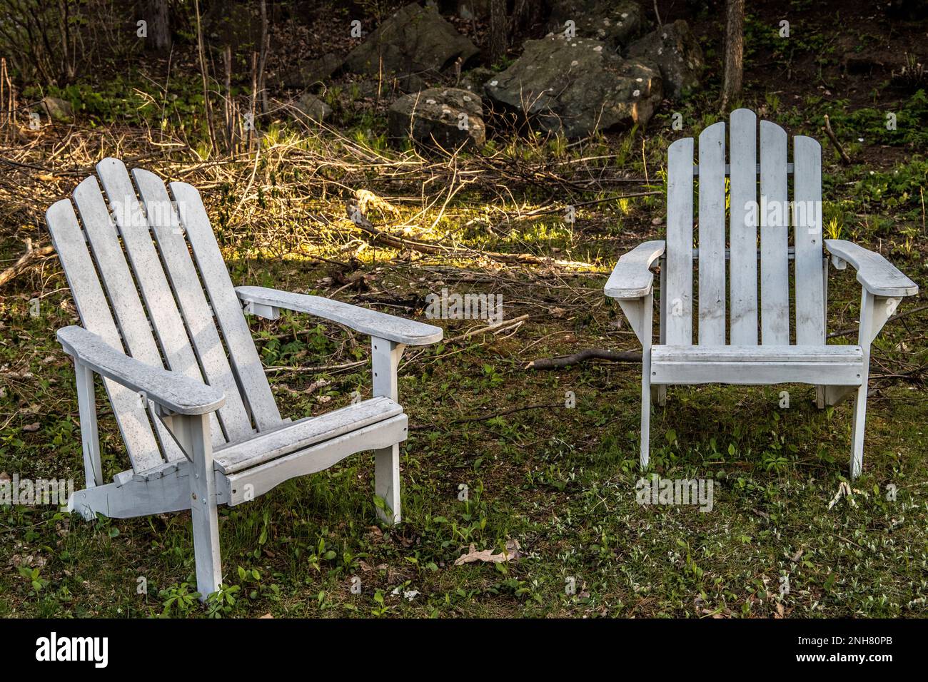 Two white Adirondack chairs with light streaming behind and rocks in