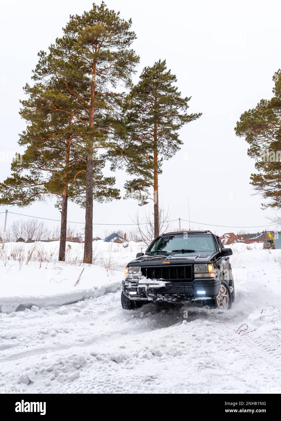 Offroad SUV 'Jeep Grand Cherokee' 4x4 with off- road training rides in winter on snow in the forest among pines with a female driver. Stock Photo