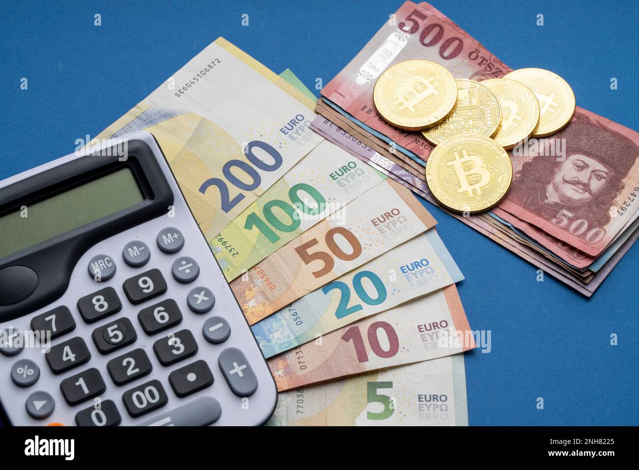 There are Hungarian forints and euro banknotes on a flat surface. A  calculator, gold blocks, and bitcoin coins are laid out next to it. HUF EUR  exchan Stock Photo - Alamy