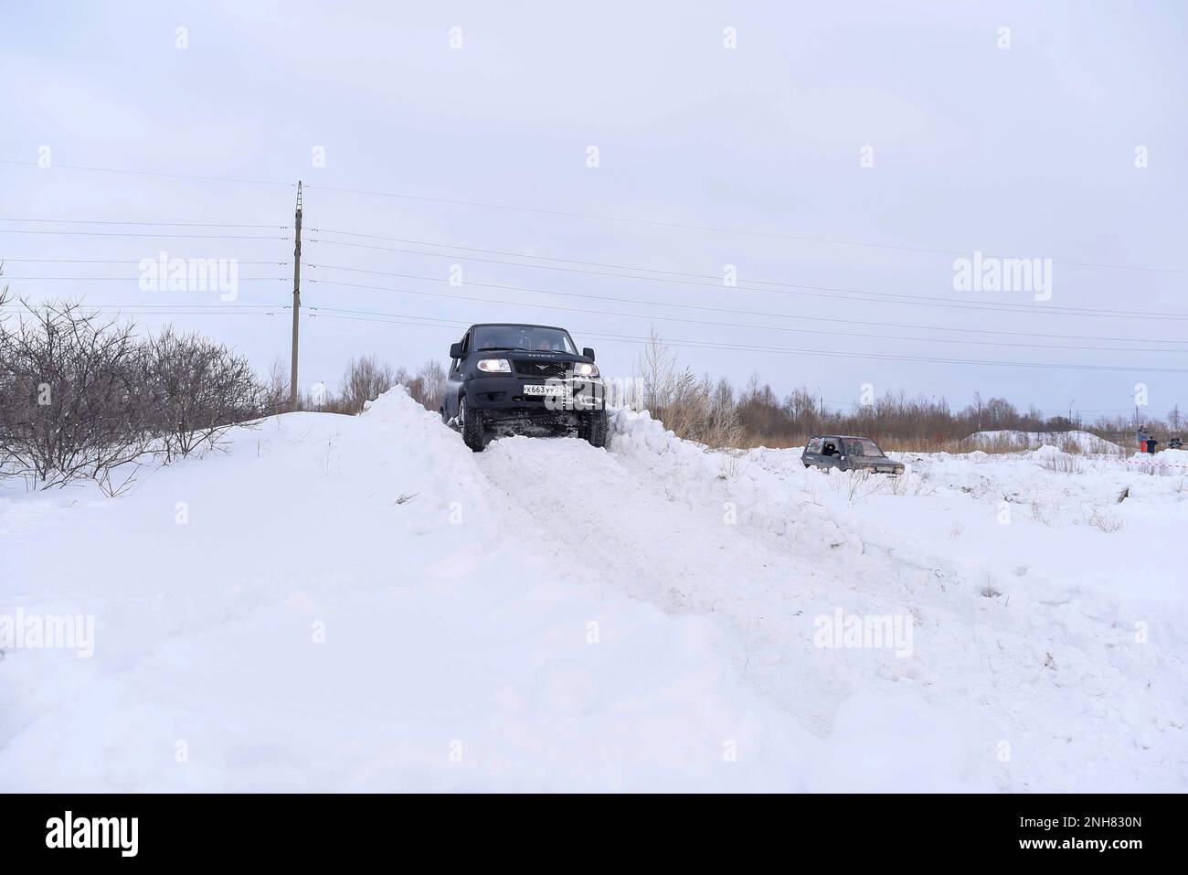 Russian SUV 'UAZ Patriot' quickly goes on a snowy road in the field in winter against the background of the forest clinging to the snowstorm wheel. Stock Photo