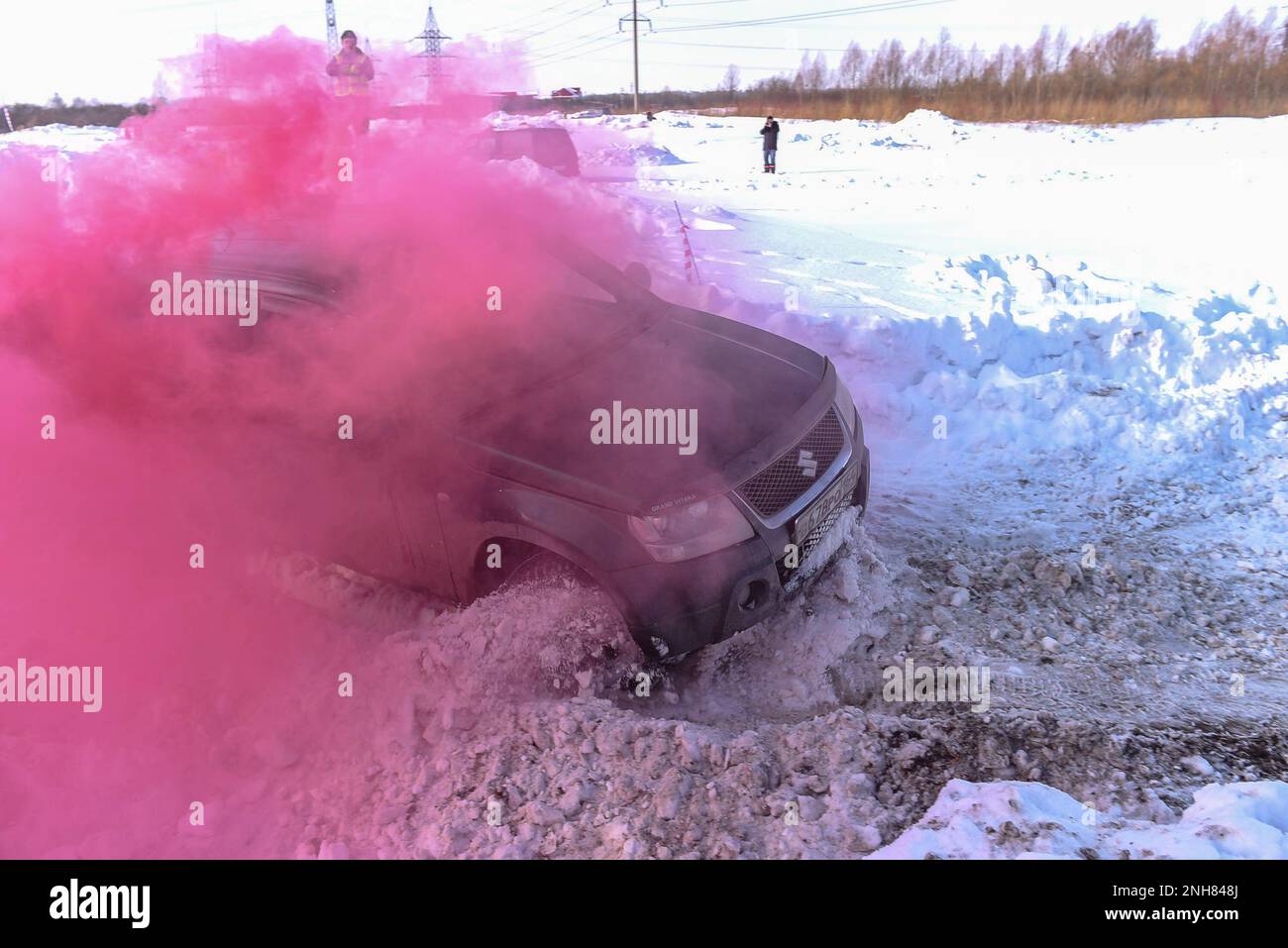 Offroad SUV 'Suzuki Grand Vitara' 4x4 is rapidly actively driving on a broken road in clouds of colored crimson smoke with snow and mud Stock Photo