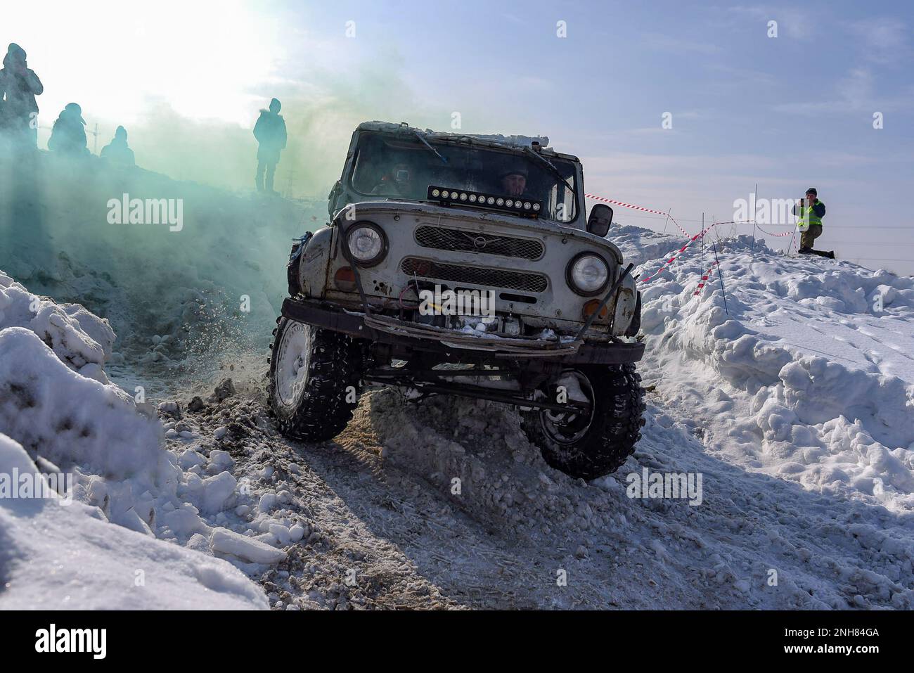 Russian SUV 'UAZ hunter 469' 4x4 goes fast, turning tires on a difficult road in the snow in winter in colored smoke. Stock Photo