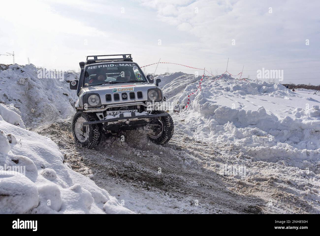 Offroad SUV 'Suzuki Jimny 4x4' quickly with a spray of Blizzard rides on a snowy road in winter on the turn turning the wheels. Stock Photo