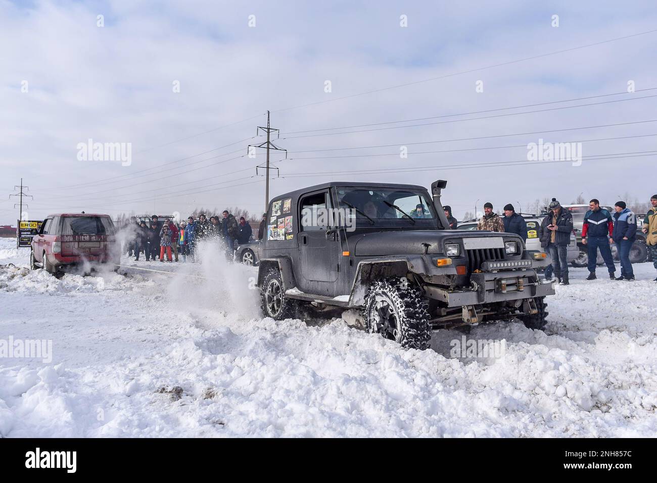 An old Jeep Wrangler skids in the snow among a crowd of people at an off-road competition in Russia in Siberia. Stock Photo