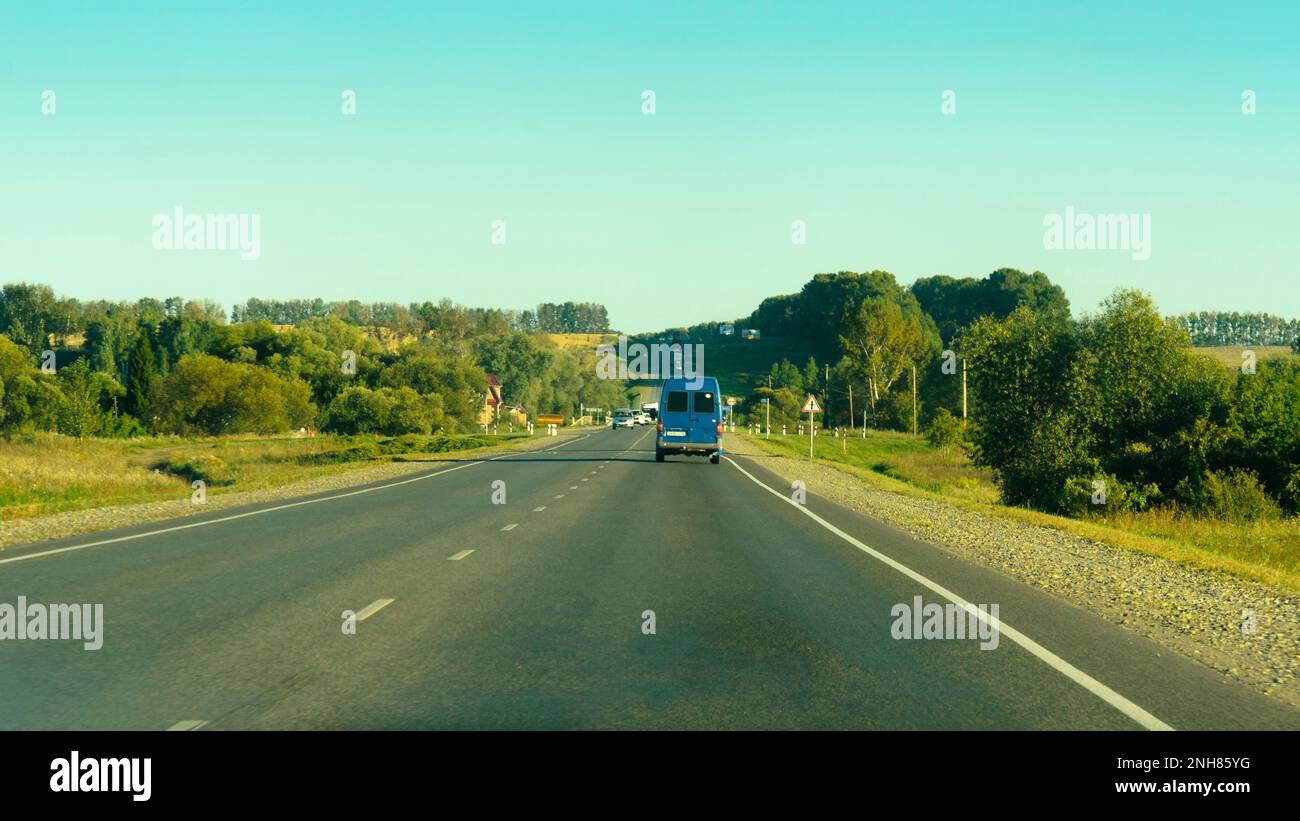 look through the car window. Unknown vechicles driving on the road among fields and woods in summer in Stock Photo