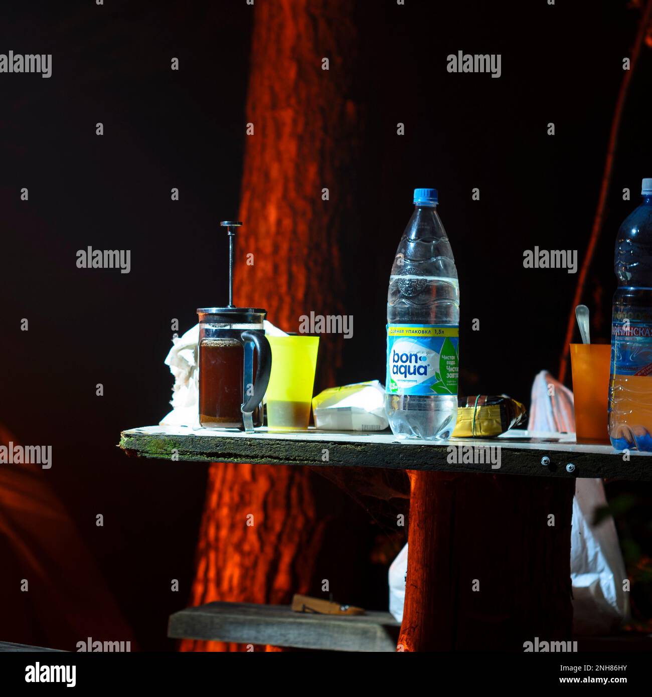 water bottle of 'BonAqua' mineral 'Karachinskaya' are on the table at night with coffee in a mug and French press around the campfire Stock Photo