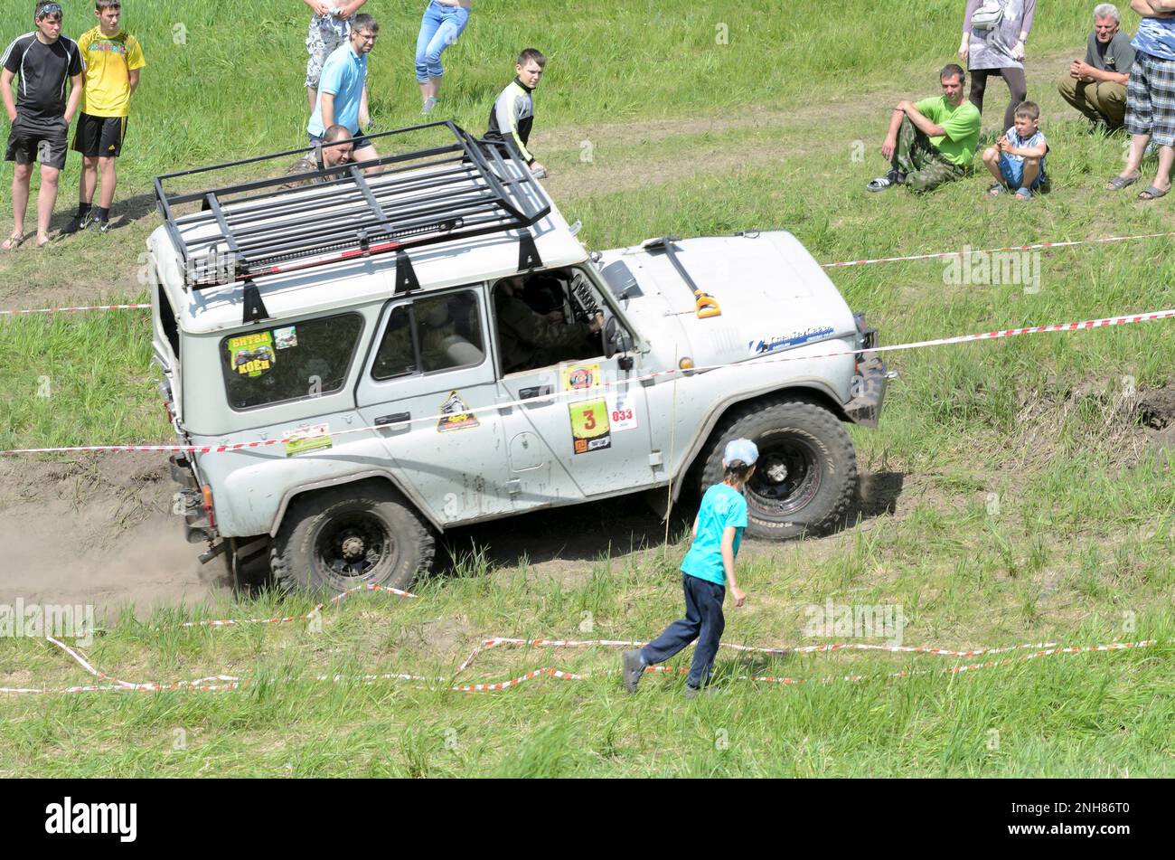 Russian military offroad car 'UAZ 469' quickly goes by the side of the mountain up past the spectators and child in Russia Stock Photo