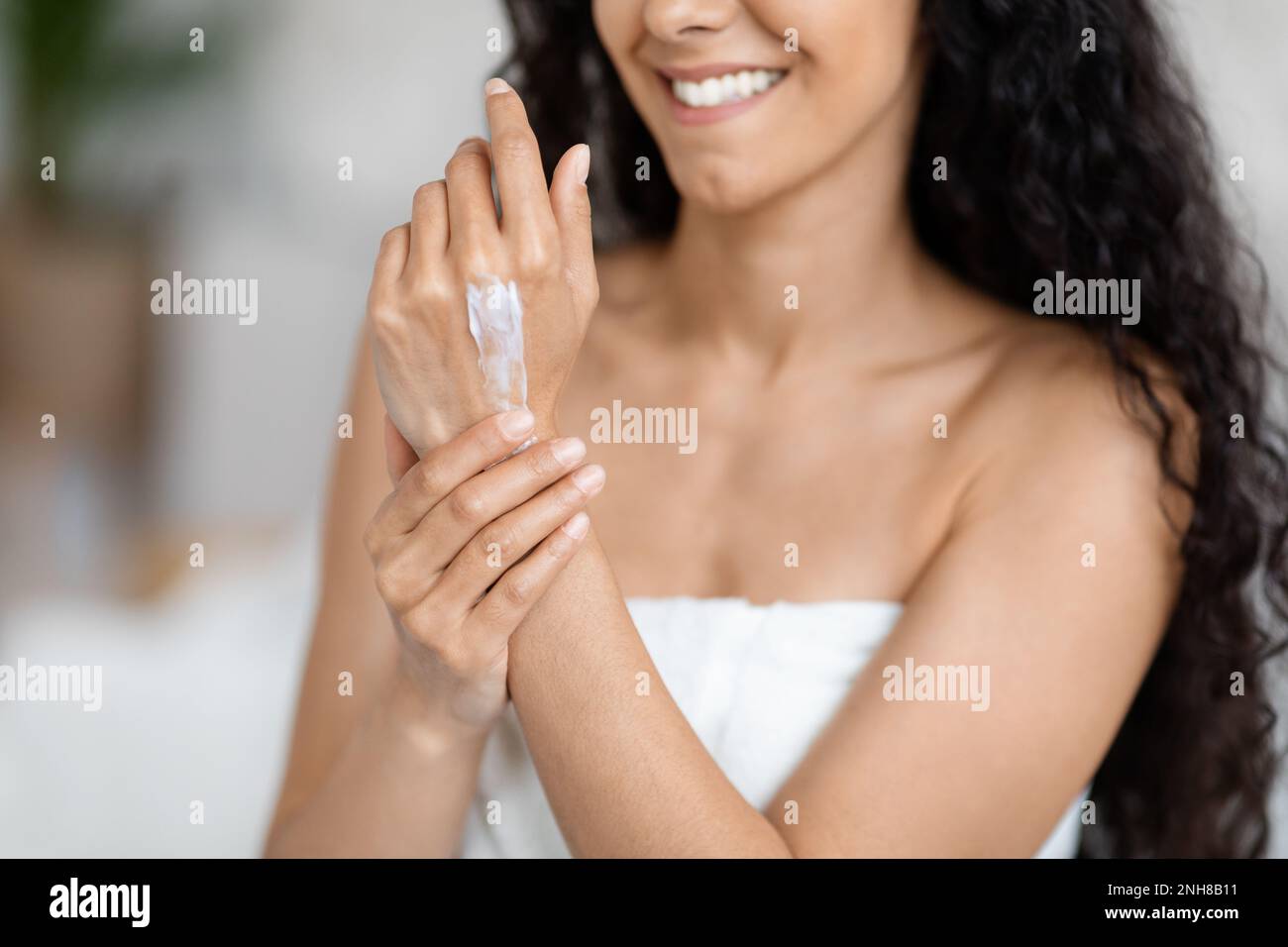 Glad millennial caucasian brunette lady with long hair in towel applies cream on hands Stock Photo