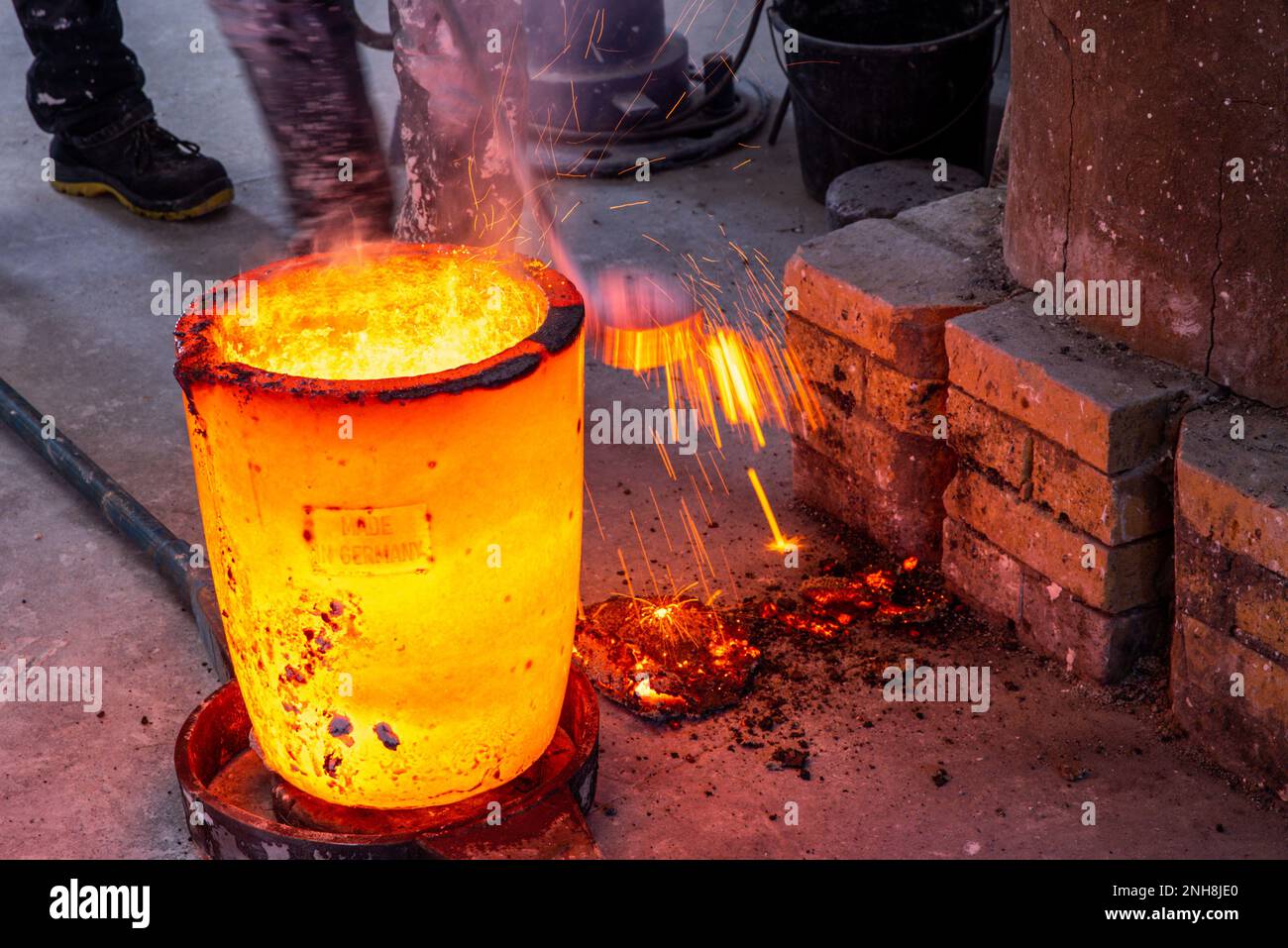 Ziesendorf, Germany. 21st Feb, 2023. Slag is skimmed off the molten bronze in a vessel at the Lachmann bronze image foundry. The molten metal is tipped into a mold to produce one of a total of eight individual parts of a Barlach monument. The Güstrow artist Henning Spitzer designed the bronze statue 'Homage to Ernst Barlach' back in 2016 and offered it to the city of Güstrow as a gift. The donation-financed sculpture, which is over two meters high, is to be erected as a monument in front of the Barlach Theater in May 2023. Credit: Jens Büttner/dpa/Alamy Live News Stock Photo