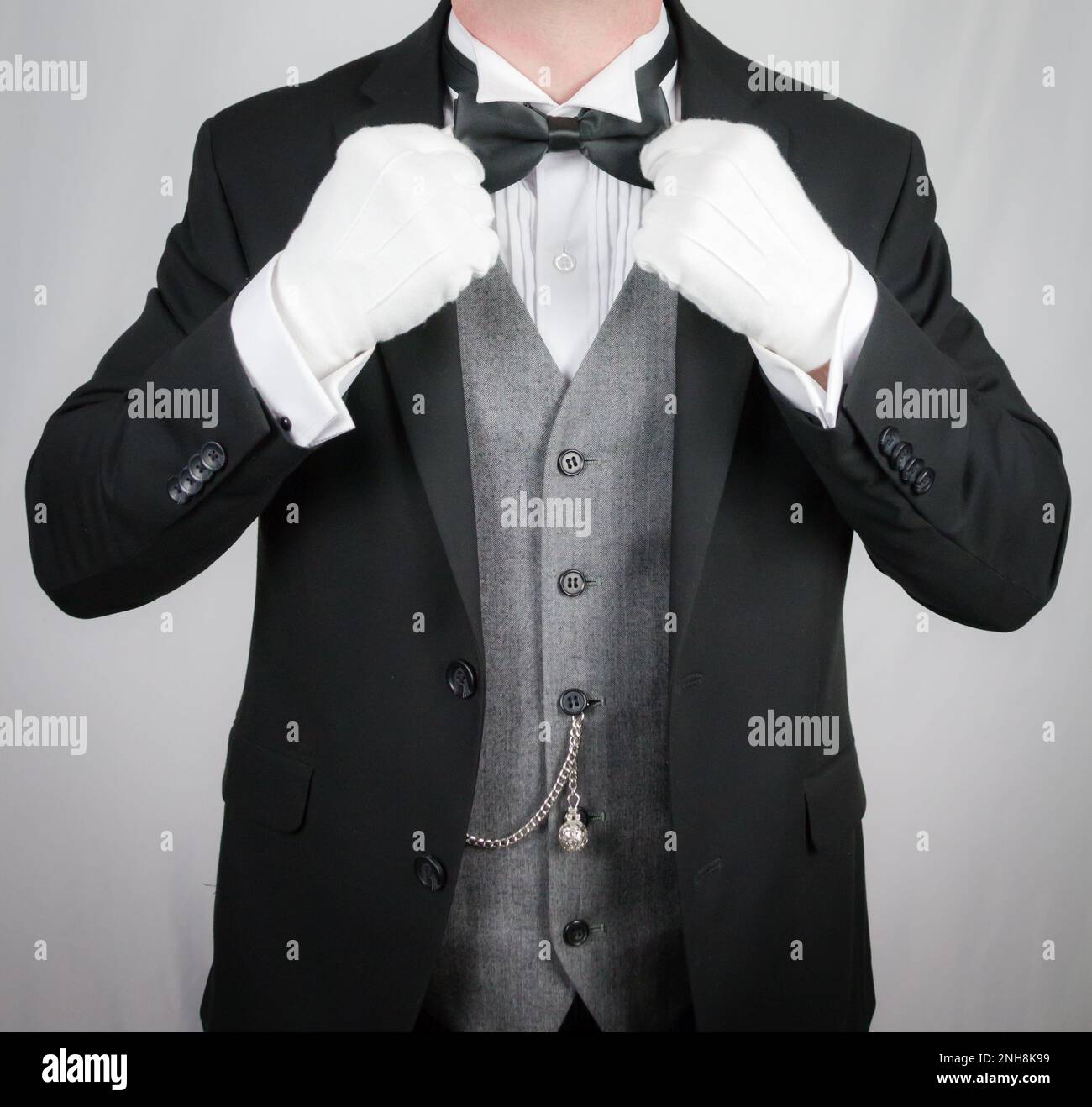 Portrait of Butler in Dark Formal Suit and White Gloves Straightening Bow Tie. Service Industry and Professional Hospitality. Stock Photo