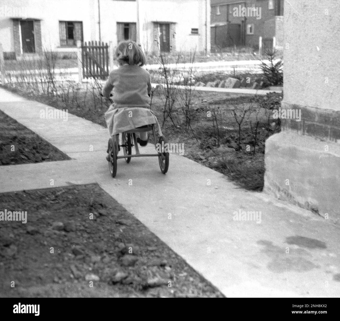 1950s, historical, view from behind of a little gilrl riding her tricycle on a recently constructed concrete path on a new housing estate, England, UK. Stock Photo