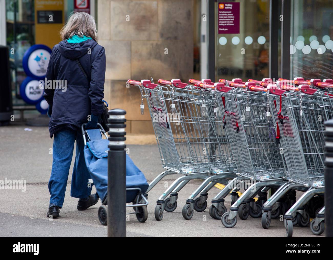 A older lady with a shopping trolley walks into Sainsbury's supermarket