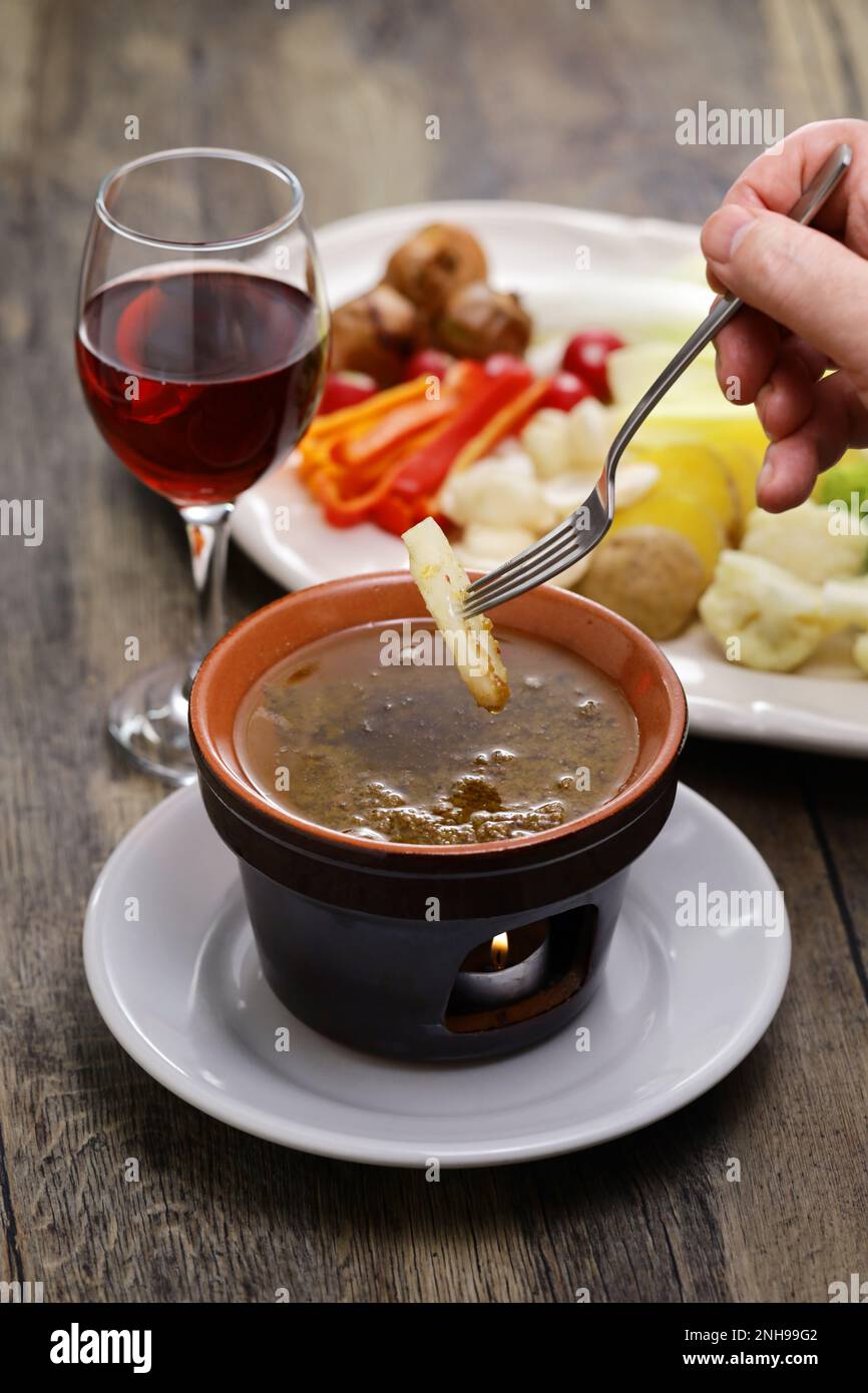 dipping jerusalem artichoke. Bagna cauda(Italian Piedmont cuisine)  is a hot dip made from garlic and anchovies. Stock Photo