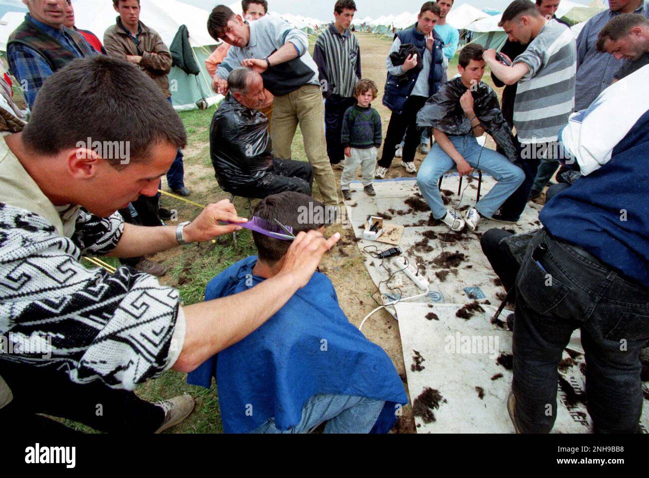 Refugees set up makeshift hair salon having arrived in Northern Macedonia via bus from the boarder crossing. Brazda refugee camp in Macedonia April 1999. The camp was run by NATO but  turned over  to UNHCR. Macedonia. Picture garyrobertsphotography.com Stock Photo