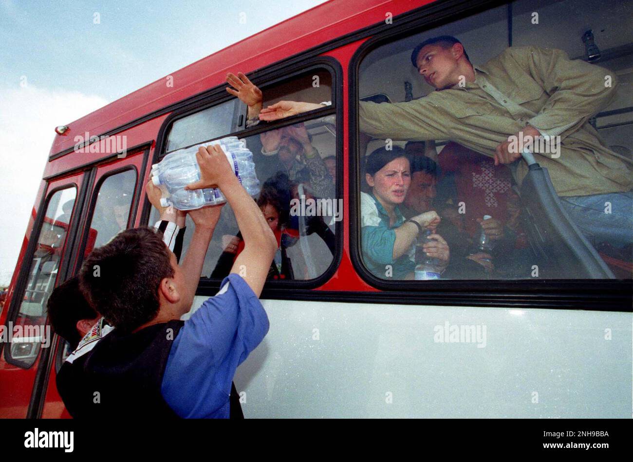 Refugees are handed water having arrived in Northern Macedonia via bus from the boarder crossing from Kosovo to Macedonia. Brazda refugee camp in Macedonia April 1999. The camp was run by NATO but  turned over  to UNHCR. Macedonia. Picture garyrobertsphotography.com Stock Photo
