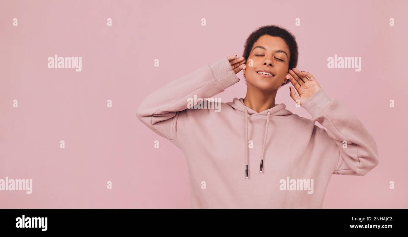 Girl standing with closed eyes and enjoying songs over pink pastel backdrop Stock Photo