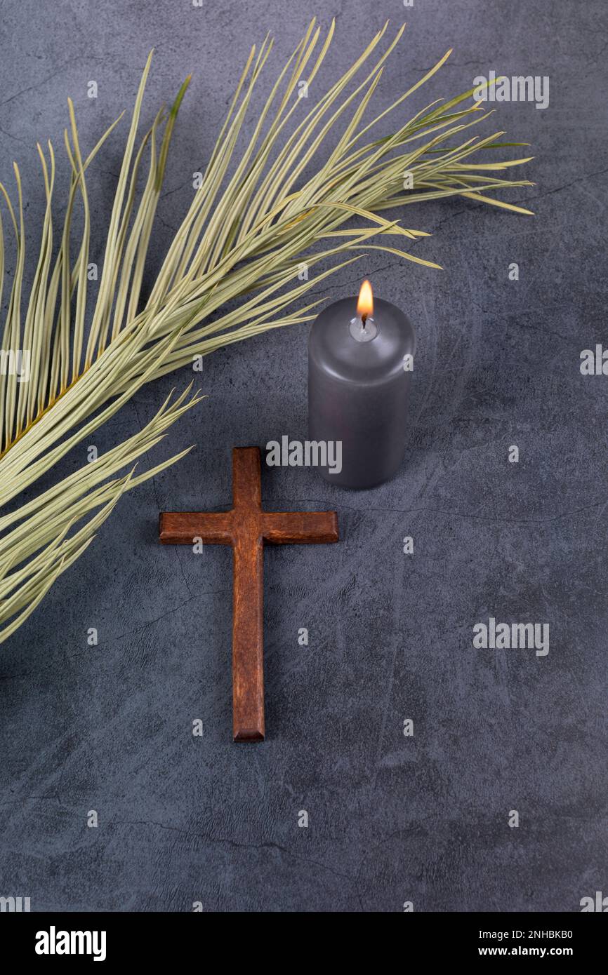 Catholic Cross with palm leaf and burning candle. Ash Wednesday, Lent season, Holy Week, Good Friday and Palm Sunday concept. Copy space. Stock Photo