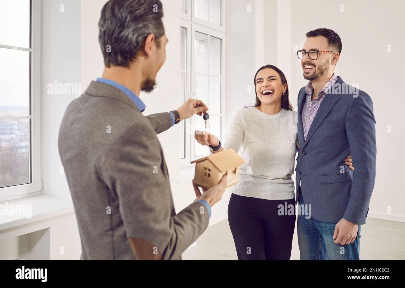 Real estate agent giving house key to a young happy smiling couple ...