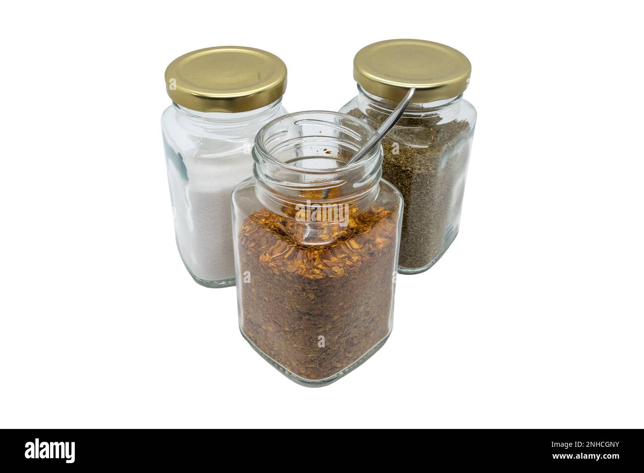 Three glass jars with spices. Chili powder with spoon, salt and celery