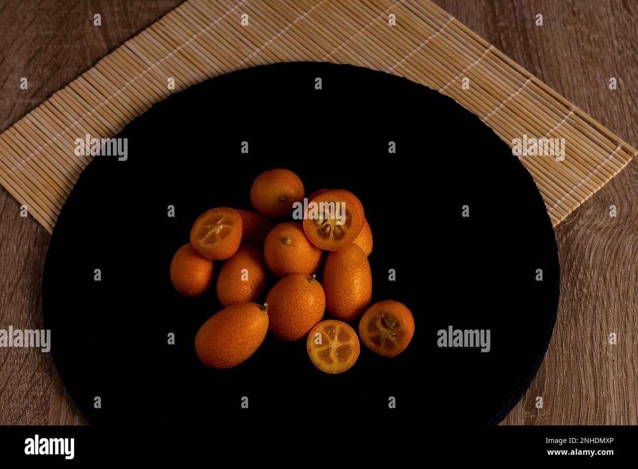 Closeup of small Chinese oranges (Citrus sinensis) or Kumquat on a black tile on a wooden table