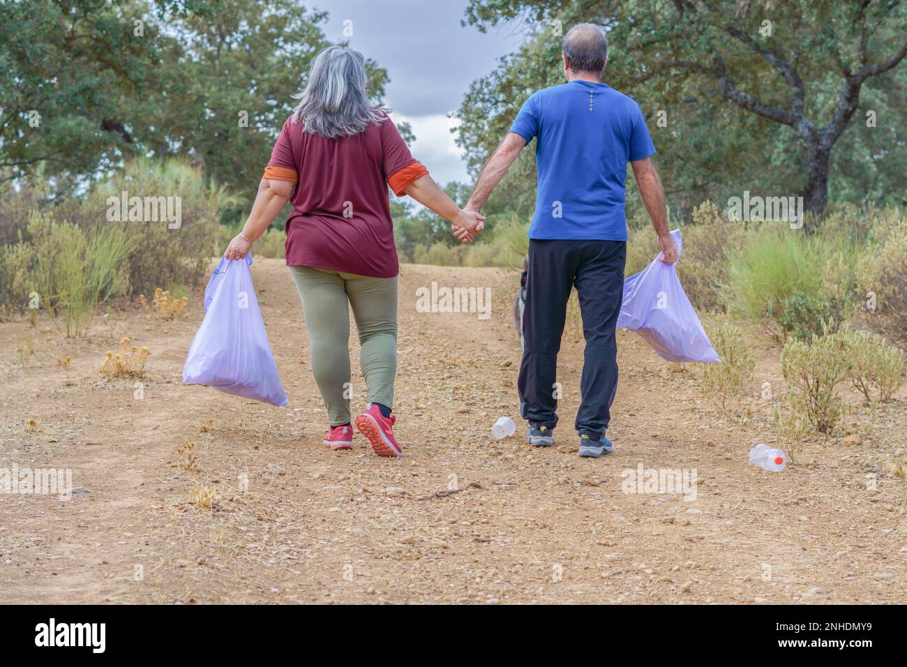 Un par de ambientalistas con bolsas de basura caminando de la mano por un camino lleno de basura Stock Photo