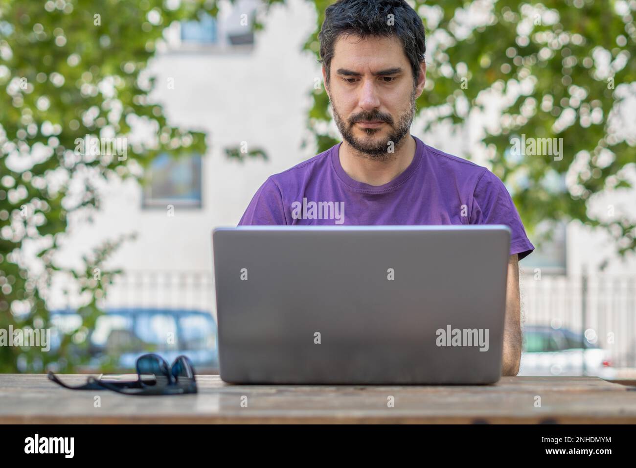 Young hypster man with beard seen from front with his pc on a park ...