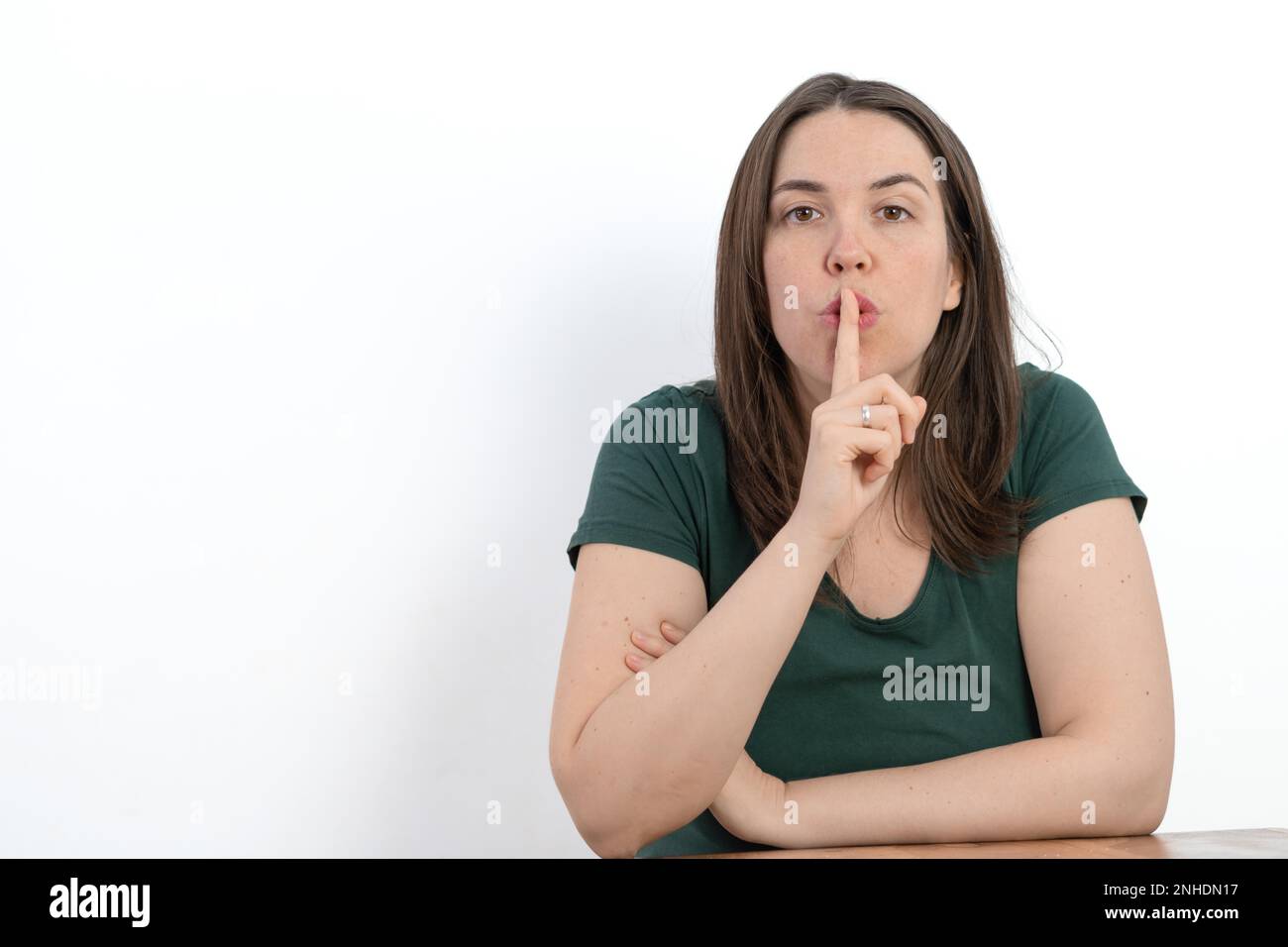 Close-up of young long-haired woman with finger in mouth asking for silence white background Stock Photo