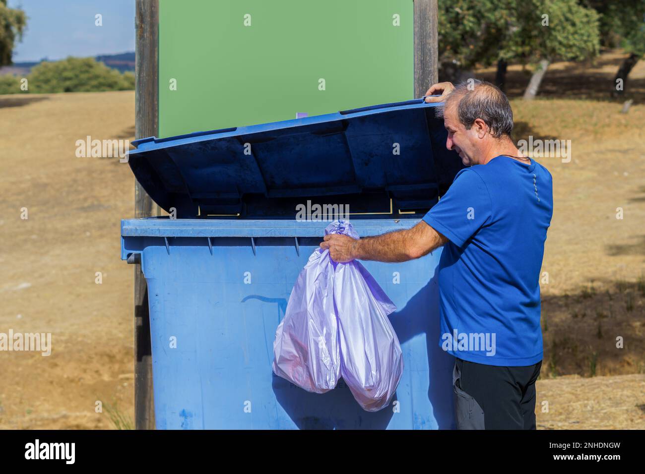 Man throwing garbage bags into a dumpster with a blank sign for copy