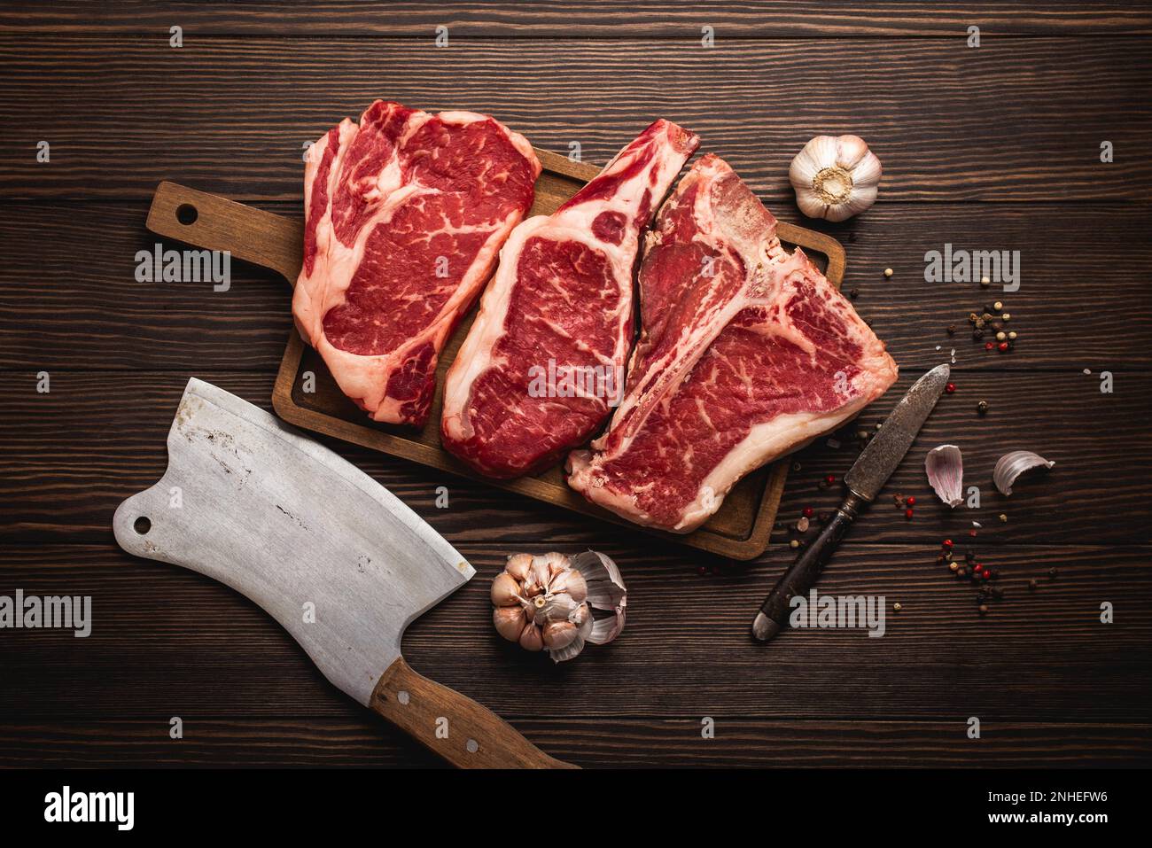 Set of three different types raw meat steaks Ribeye, Tbone, Cowboy on cut board with knife and