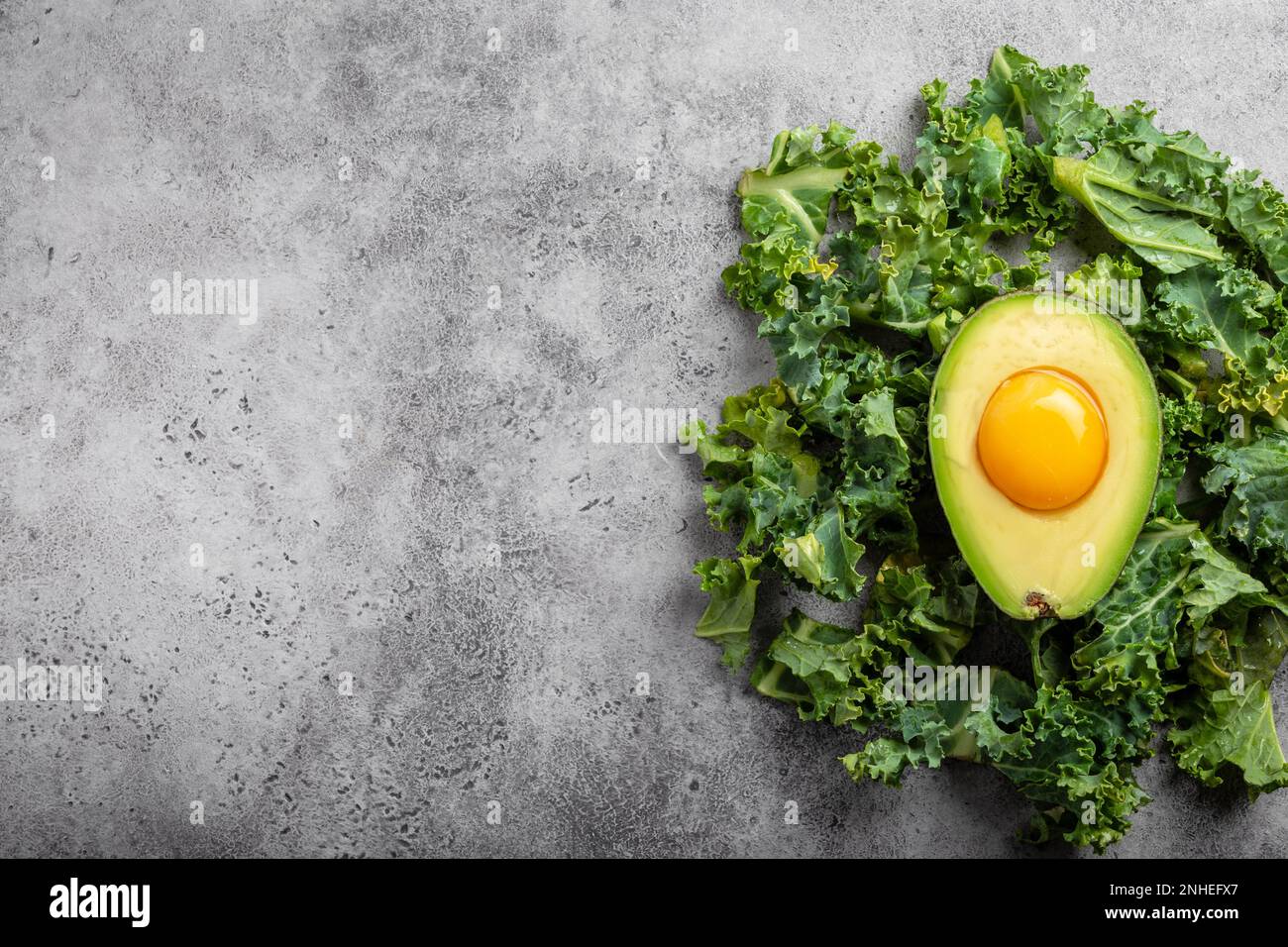 Raw egg yolk in fresh cut half avocado rich in healthy fats and kale