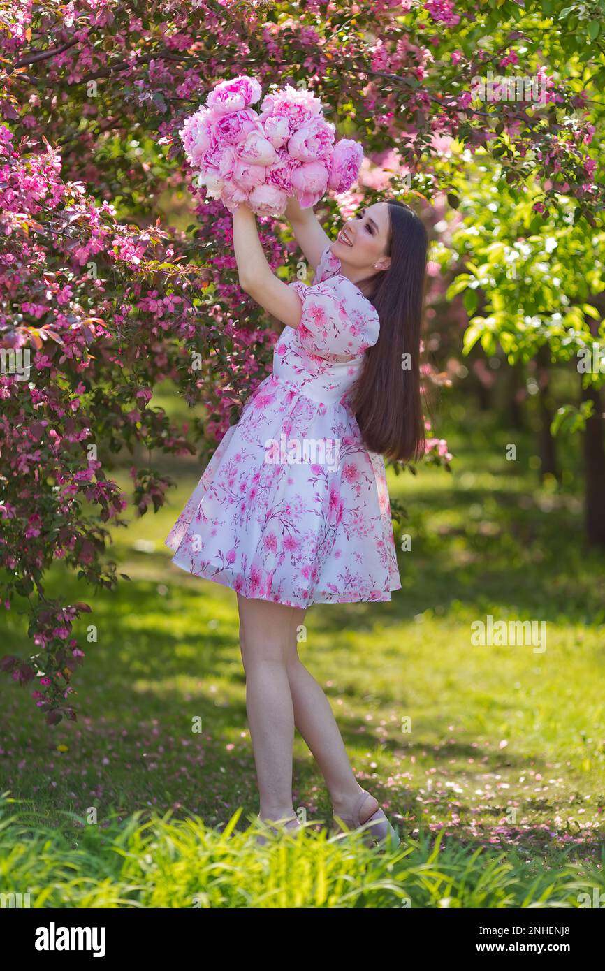 A smiling girl in a light pink dress, with a bouquet of large pink ...