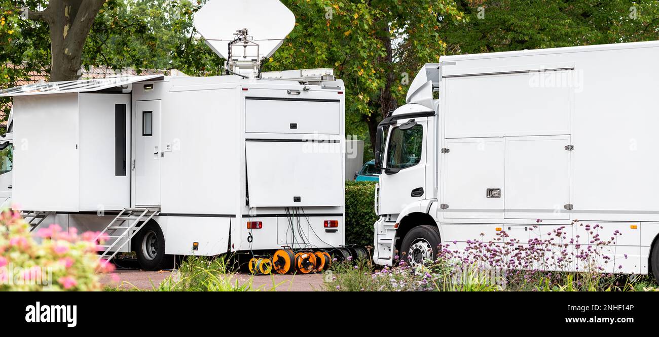 Many modern white mobile digital electric tv broadcasting trucks satellite antenna live streaming online breaking news sport channel city park Stock Photo