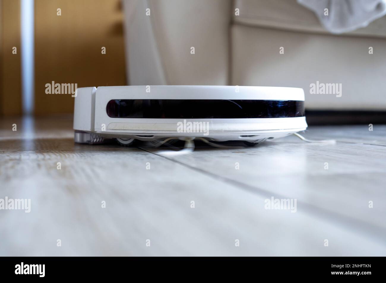 white robot vacuum cleaner cleans the room near the doors and the sofa