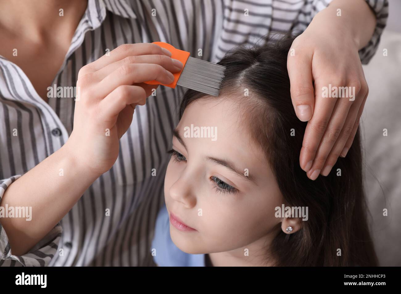 Mother using nit comb on her daughter's hair indoors. Anti lice