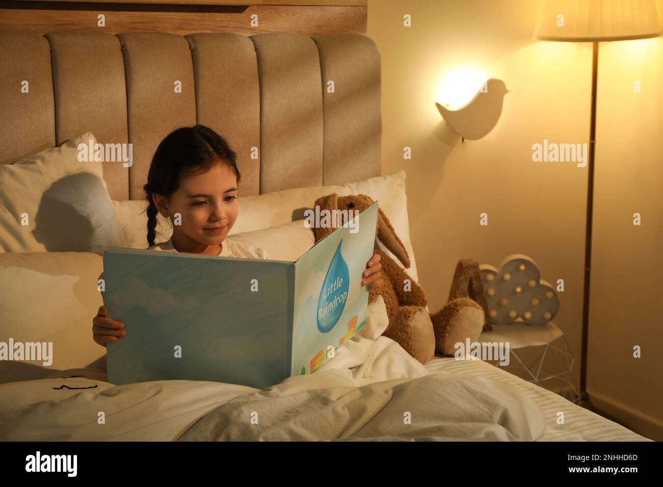 Little girl reading book in bedroom lit by night lamp Stock Photo