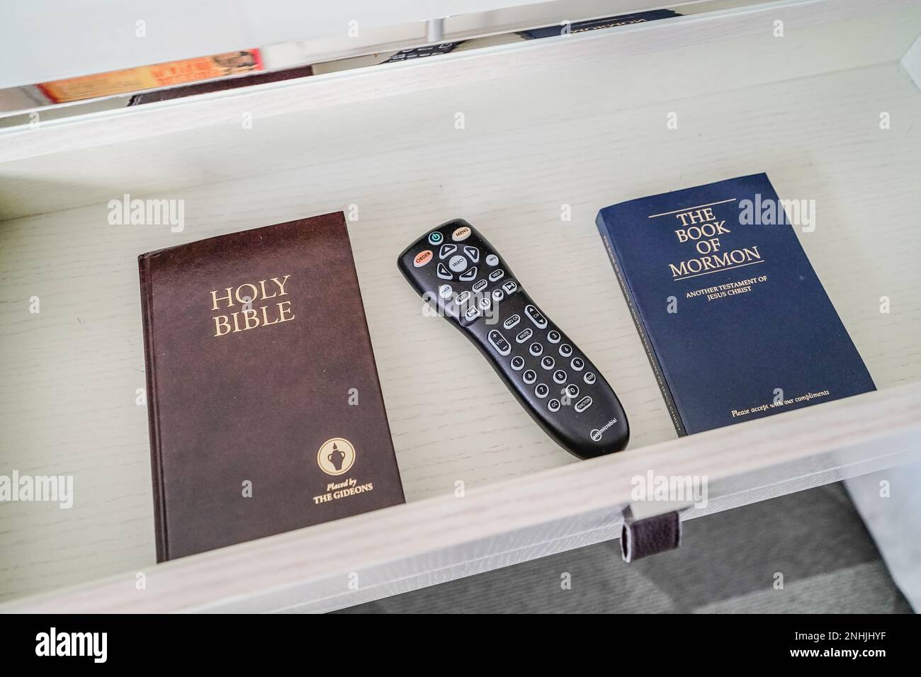 holy bible, book of mormon and tv remote inside the drawer of a hotel